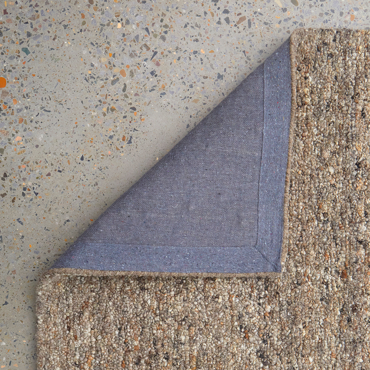 Turned-back corner of Conscious Loom Embrace Runner Stone highlighting the backing detail and chunky wool texture in stone, beige and cream tones