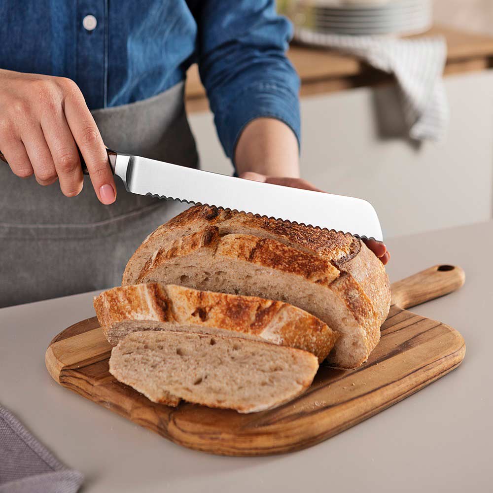 woman cutting slices of bread with bread knife at kitchen counter - MyHouse