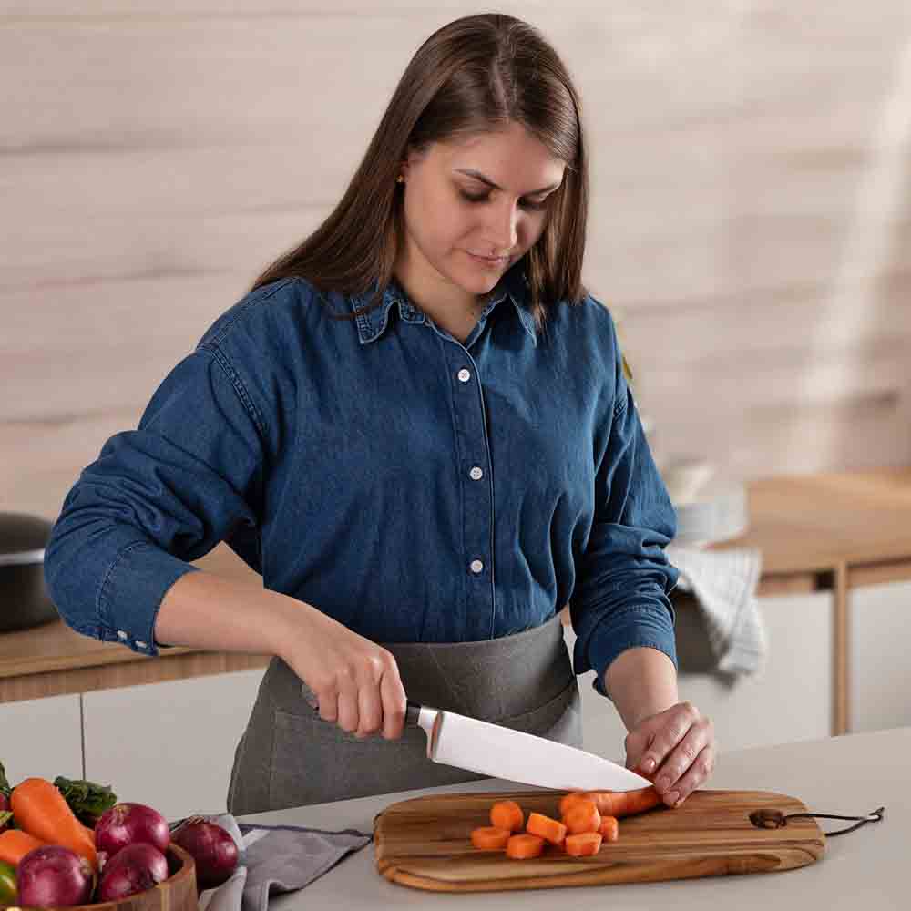 woman chopping carrot at kitchen counter with chef knife - MyHouse