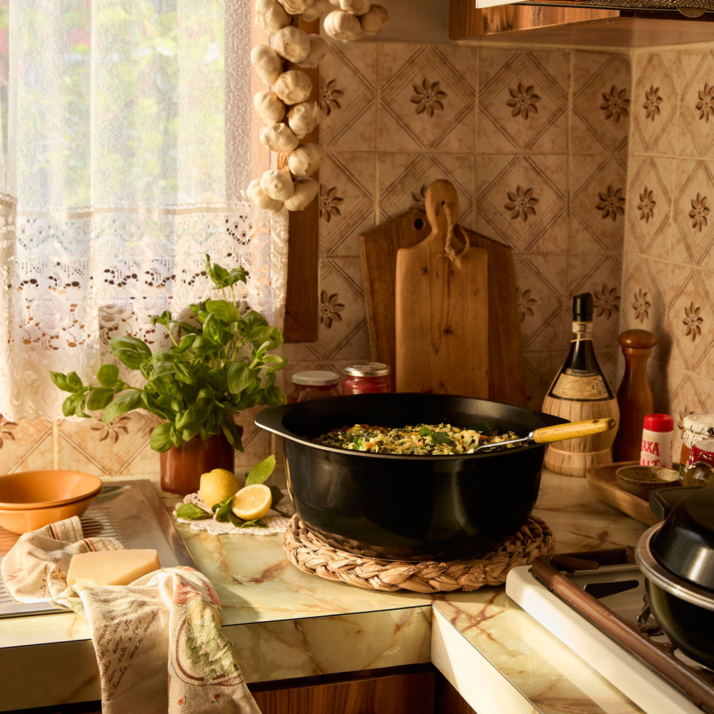 Kitchen counter with a pot of food, lemons, and a plant on a tiled backsplash.