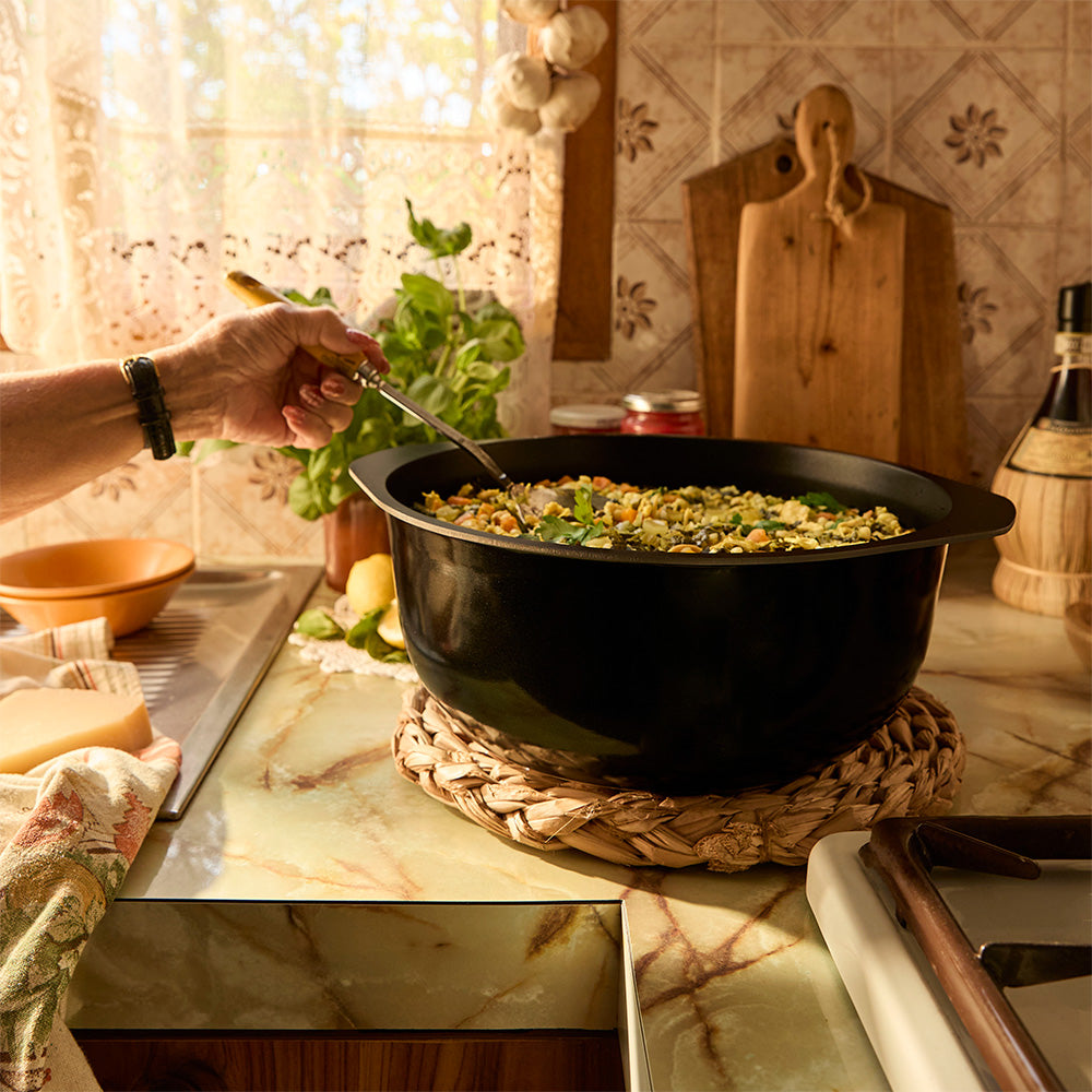 Person cooking in a kitchen with a black pot on a marble countertop.