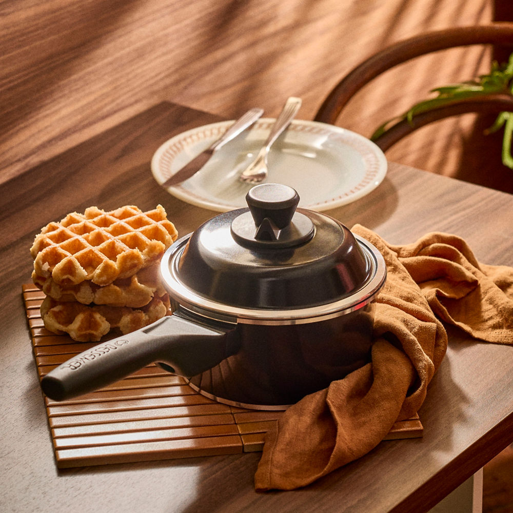 Stack of waffles next to a waffle iron on a wooden table