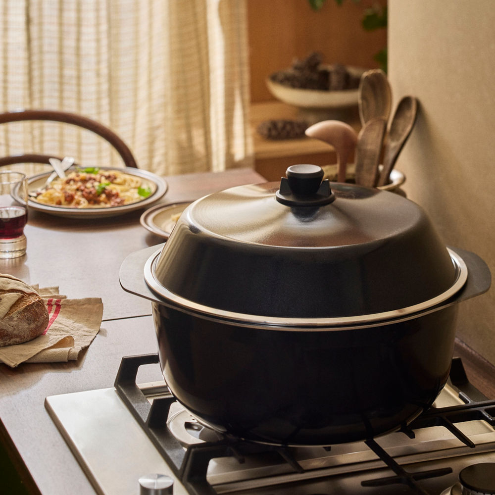Black pot with a lid on a stove, surrounded by a meal and utensils in a home setting.