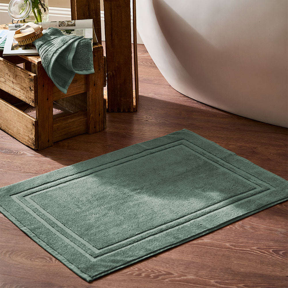 MyHouse Celene Egyptian Loop sage bath towel collection styled with colour-matched bath mat beside a freestanding bathtub