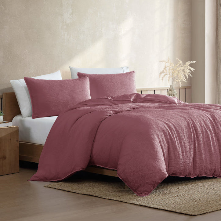 Pink bedding set on a bed in a bedroom with a window in the background