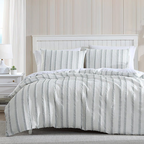 Bedroom with a neatly made bed featuring a striped comforter, nightstand, and bookshelf.