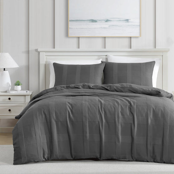 Gray bedding set on a bed in a bedroom with white walls and a window.