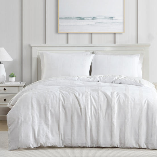White bedding set on a bed in a bright bedroom with neutral decor.