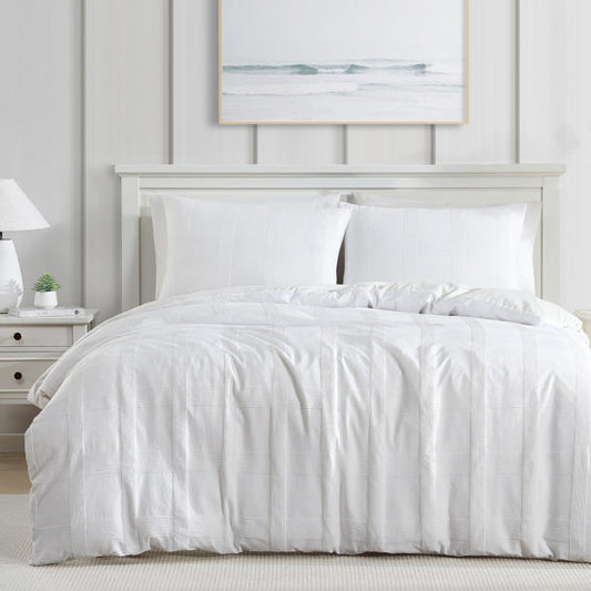 White bedding set on a bed in a bright bedroom with neutral decor.