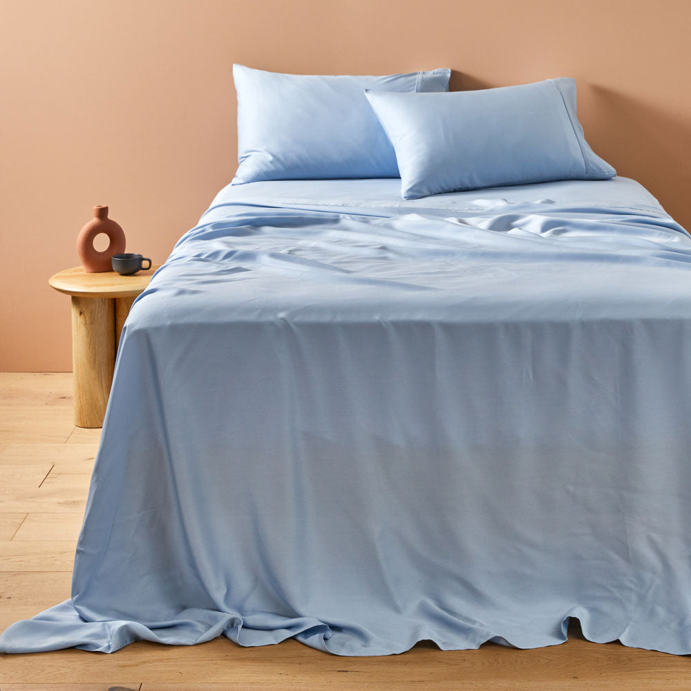A blue Lyocell sheet set on a bed, including a fitted sheet, a flat sheet, and two pillowcases.