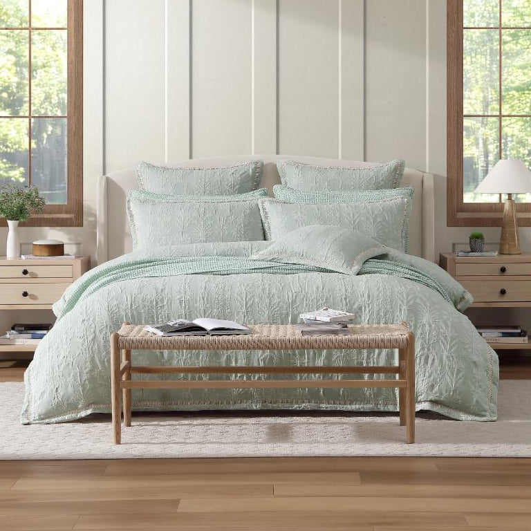 Bedroom with light green bedding and wooden bench