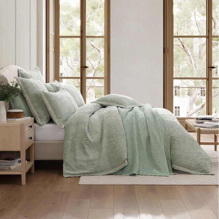 Bedroom with light green bedding and wooden furniture.