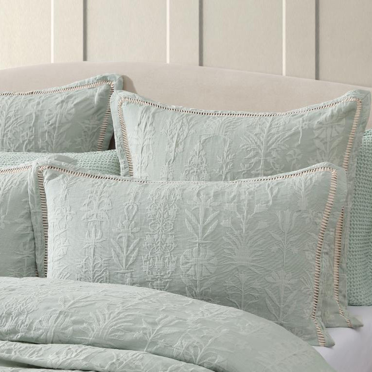 Light green quilted bedding set on a bed with a neutral headboard.