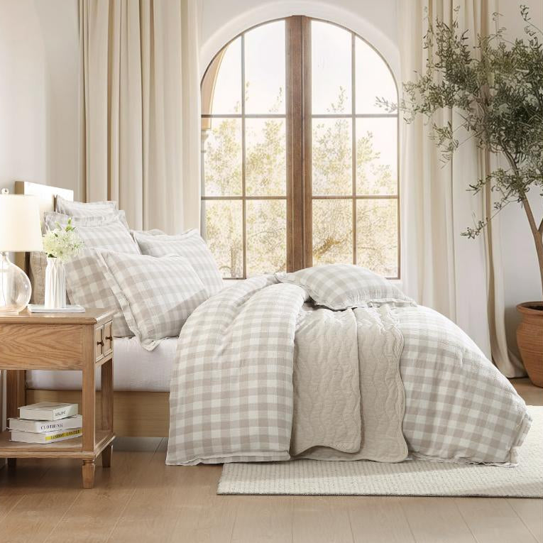 Neatly made bed with checkered bedding in a bedroom with large windows and curtains.