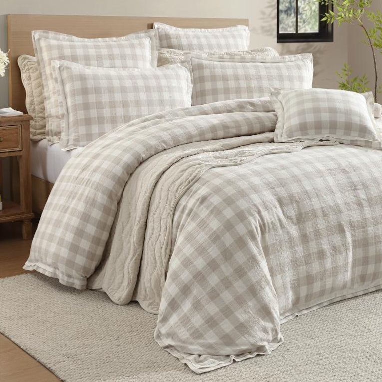 Plaid bedding set on a bed in a bedroom with a window and plant in the background.