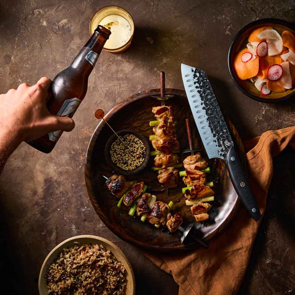 Man pouring beer beside Baccarat KUROI KIBA Santoku Knife 18cm at MyHouse