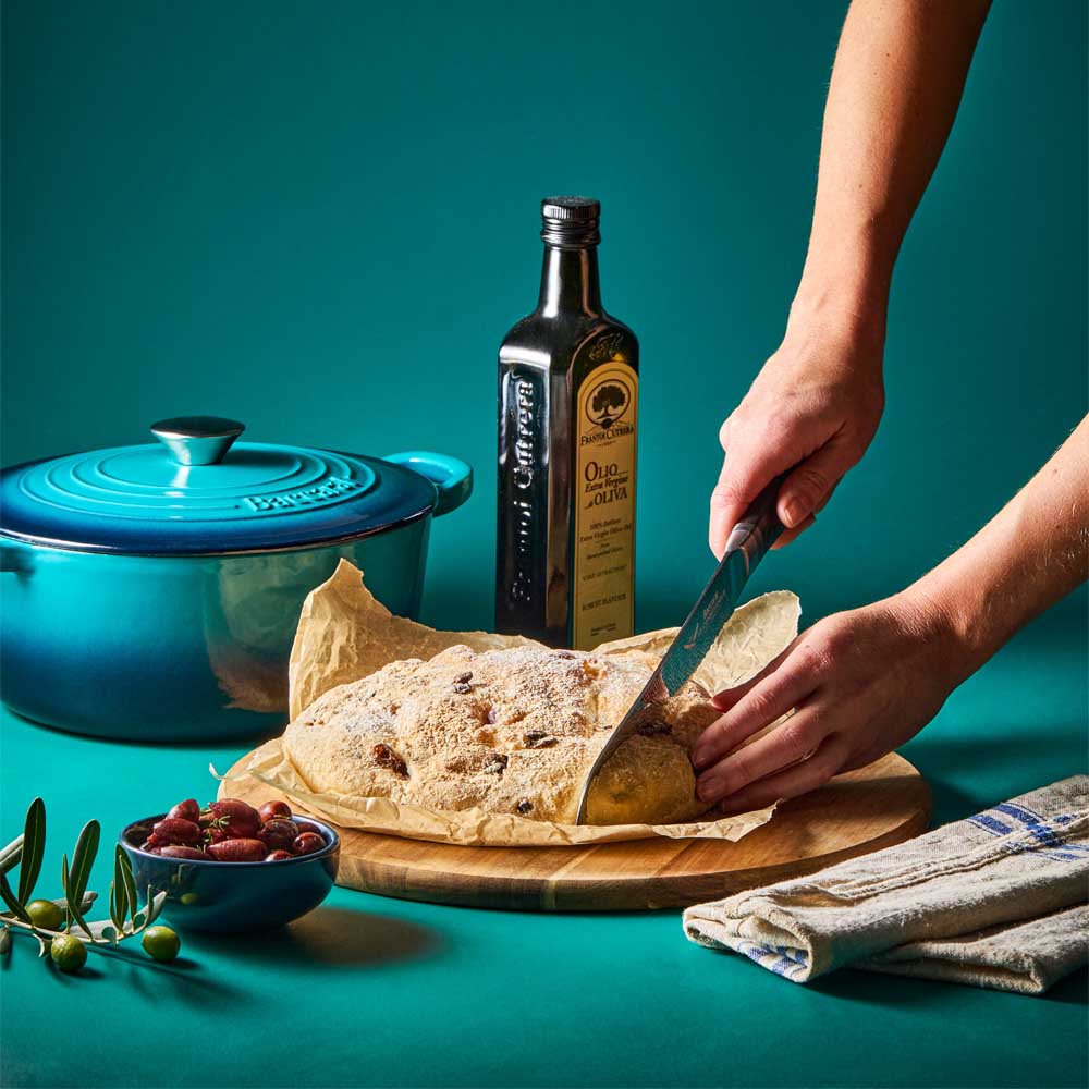 woman cutting bread baked from blue french oven - MyHouse